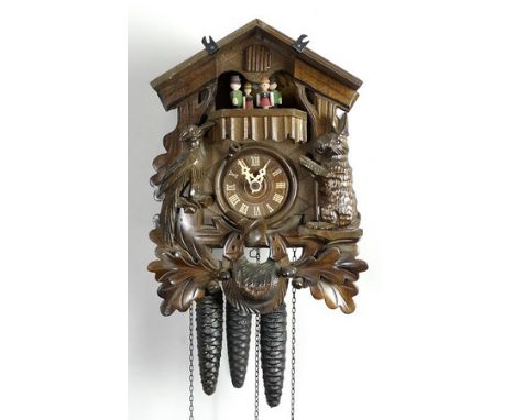 A Black Forrest cuckoo clock of carved wood with a carousel of four children below the cuckoo, and complete with chain and fo