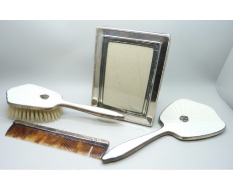 A silver photograph frame, a silver and enamelled hand mirror and brush and a silver mounted comb 