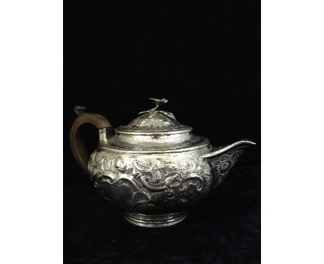 A Georgian silver teapot of melon form with wooden loop handle on circular foot with all-over embossed floral decoration by S