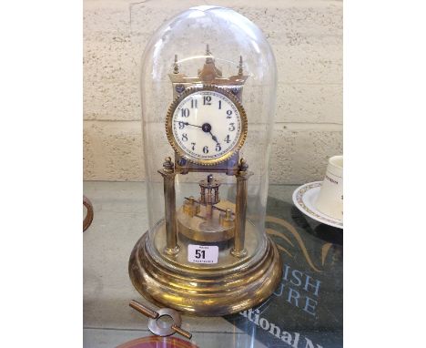 A brass skeleton clock with disc pendulum, white enamel face with Arabic numerals under glass dome on circular brass base.