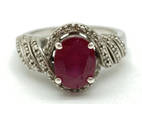 A silver ruby and diamond cocktail ring. Central oval cut  ruby in decorative pierced illusion mount, with twist design shoul