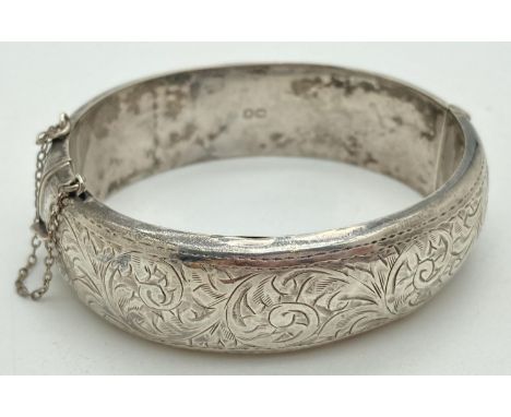 A vintage silver hinged bangle with half engraved foliate and scroll detail. Safety chain in tact and clasp shuts firmly. App