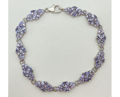 A silver cocktail bracelet set with 11 floral design panels set with tanzanite stones. Each panel set with 4 marquise cut and