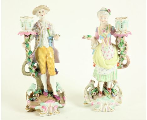 A pair of attractive German porcelain Candlestick Groups, early 20th Century, one modelled as an elegant woman holding a flor