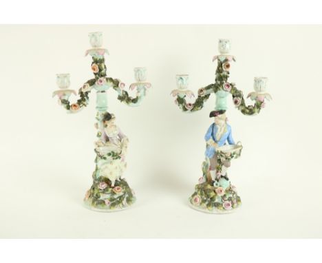 An attractive pair of flower encrusted Sitzendorf two branch three light Candelabra, one modelled with a man holding a basket