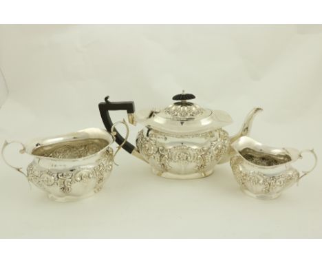 A three piece silver Tea Service, Birmingham 1907, comprising an embossed oval teapot with hinged cover and ebonised handle; 