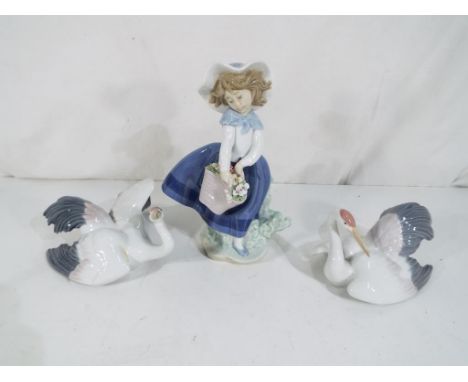 Lladro - Three figurines by Lladro to include a girl carrying a basket of flowers and two models of cranes comprising 1599 an