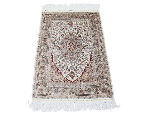 A Hereke silk carpet, with central shaped lozenge with trailing tendrils and flowerheads on pale cream ground, with floral bo