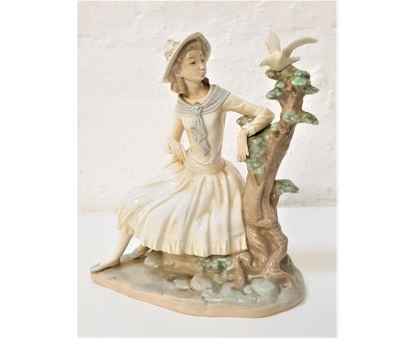 NAO PORCELAIN FIGURINEof a young girl seated by a tree looking at a dove, 24cm high 