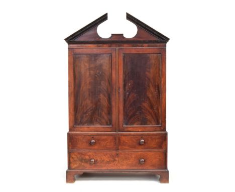 A late Georgian mahogany linen press, extravagant broken pediment with dentil detail, over two doors opening to a hanging rai