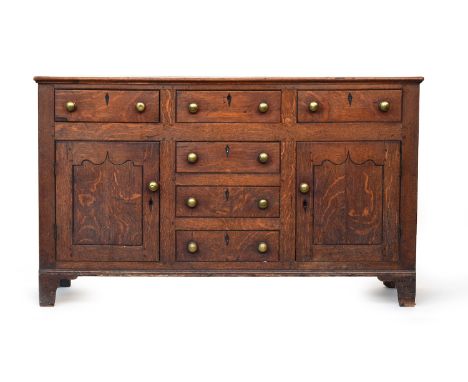A George III oak dresser base, having three short drawers and a further three drawers flanked by cupboards, brass knobs, on b