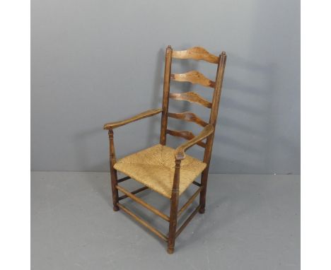 An antique oak rush seated ladder-backed open armchair.