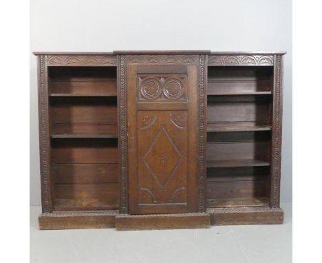A Jacobean style carved oak breakfront bookcase, the single cupboard with shelf fitted interior flanked by open adjustable bo