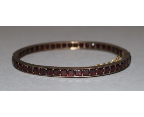 An Edwardian gold and garnet set hinged bangle,