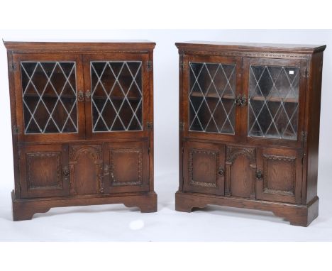 A PAIR OF REPRODUCTION GLAZED OAK CUPBOARDS WITH PAIR OF LEADED DOORS ABOVE PANELLED CUPBOARDS AND ARCADED CENTRAL PANEL, BRA