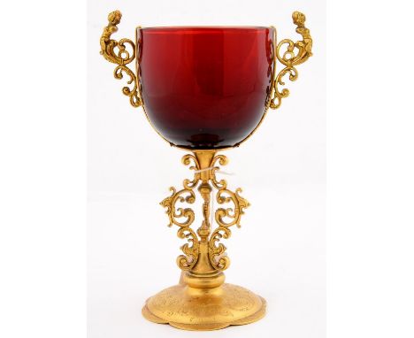 A GERMAN MANNERIST STYLE GILTMETAL MOUNTED RUBY GLASS CUP, LATE 19TH C, IN 16TH C STYLE, WITH CARYATID HANDLES, ON THREE SCRO