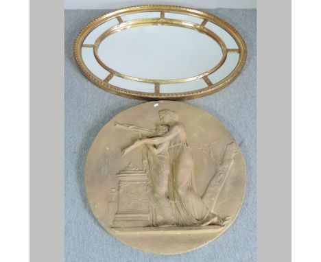 An oval gilt framed wall mirror, with marginal surround, 110 x 86cm, together with a marble effect roundel plaque, decorated 