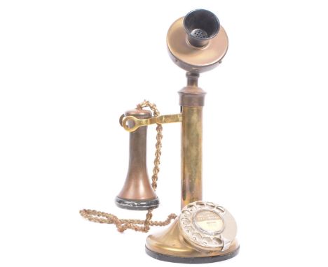 An early 20th century brass candlestick telephone. The telephone of brass construction with black bakelite elements to mouthp