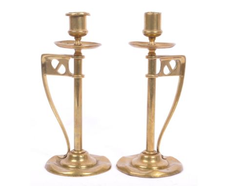 A pair of early 20th century arts &amp; crafts / Art Nouveau brass candlesticks. Having scalloped bases with pierced handles.