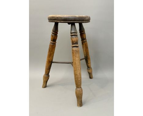 An early 20th century beech and elm tripod stool - with concave circular seat and turned supports with baluster feet united b