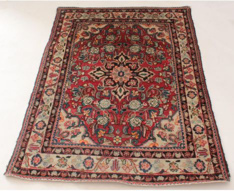 A Persian Sarouk hand-knotted wool rug - first half 20th century, the dark-blue four-point floral medallion on a red ground w