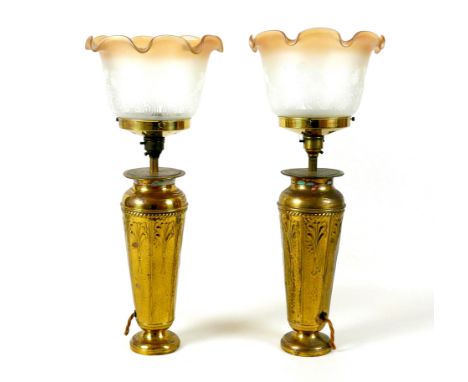 A pair of Art Nouveau brass table lamp bases, with embossed floral decoration, frosted glass shades with frilled rim. (2) 