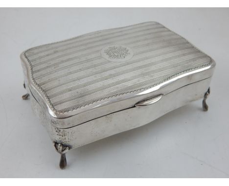 A late Victorian white metal trinket box shaped rectangular, the hinged engine turned cover with central monogram, on four sc