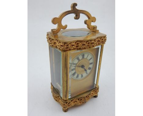 A brass cased carriage clock, scroll pierced applied borders with hinged scrolling handle, the enamel dial with Roman numeral