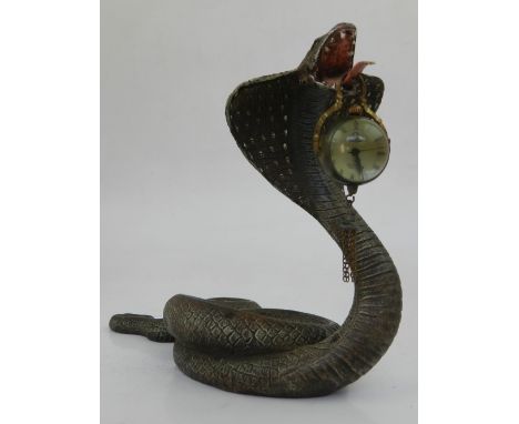 A cold painted bronze watch stand in the form of a cobra, carrying a suspended ball clock in its mouth.