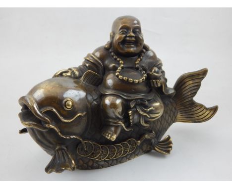 A cast bronze sculpture of Buddha riding a fish. 