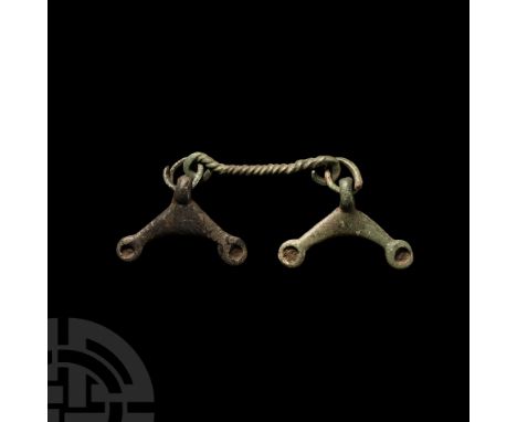 Circa 1st century B.C.-1st century A.D. or later. Composed of a twisted bar with pendant dangle to each terminal formed as sh