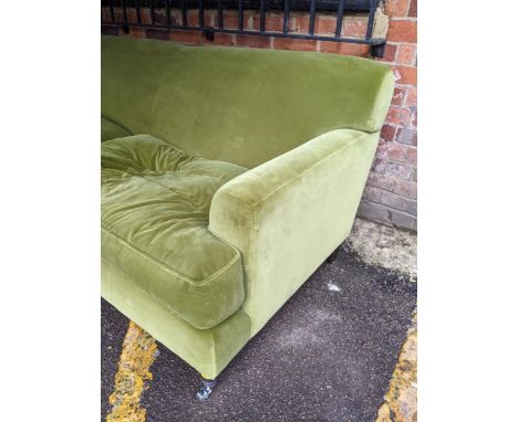 An upholstered three-seater sofa in plush green velvet fabric with matching loose seat cushions, on black coloured turned fro