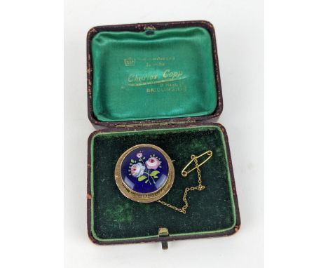 An early 20th century 9ct gold and enamel on copper brooch, decorated with roses on a blue ground, 3cm dia with a safety chai