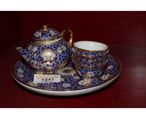A Child's or doll's porcelain miniature tea service, decorated in gilt and blue with flowers, comprising tea pot, three tea b