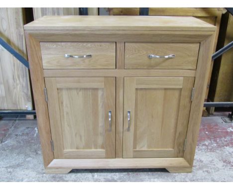 An Oak Furniture Land light oak side cupboard, the bevelled front enclosed by a pair of rectangular panelled doors beneath tw