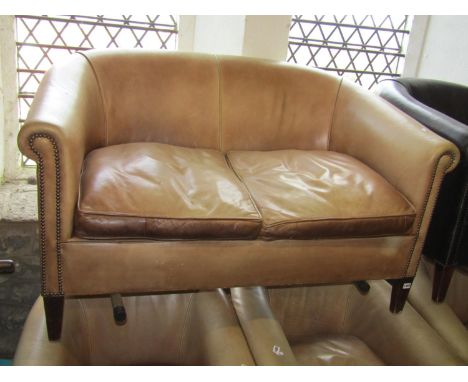 A leather two-seat sofa, with rolled arms and brass studded borders, covered in weathered tanned leather