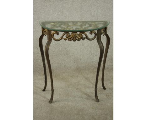 A contemporary gilt cast iron console table, of demi lune form with a plate glass top, the body formed of scrolling leaves, o