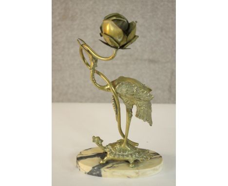 An Oriental brass candlestick in the form of a figure of a stork holding a flower, standing on a tortoise mounted on a marble