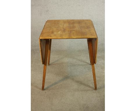 An Ercol light elm drop leaf dining table, with two drop leaves on splayed beech legs, maker's labels to the underside. H.71 