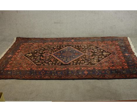 A hand made red ground Persian Hamadan carpet with central lozenge medallion within stylised flowerhead multiple borders. H.2