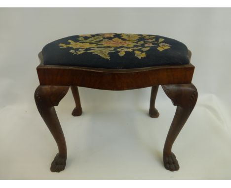 An early 20th Century walnut shaped stool with tapestry drop in seat, raised upon cabriole supports to hairy paw feet.