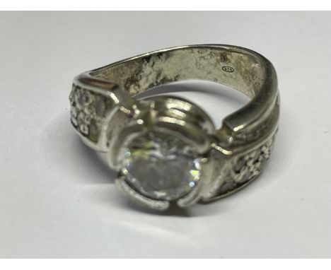 A SILVER RING WITH A LARGE CENTRAL CLEAR STONE AND CLEAR SONES ON TWISTED SHOULDERS SIZE O/P IN A PRESENTATION BOX 