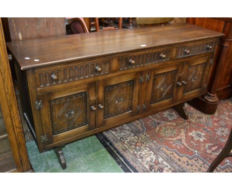 A Priory style oak sideboard, oversailing top, three fluted front short drawers over four carved panel door cupboard to base,