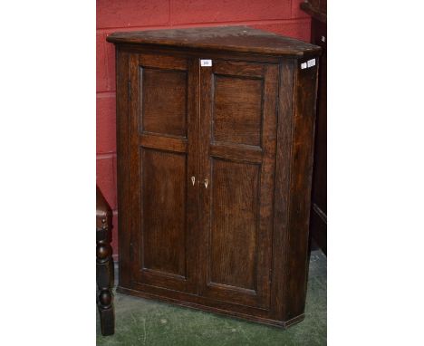 A George III elm and oak splay fronted wall hanging corner cupboard, moulded cornice above a pair of panelled doors enclosing