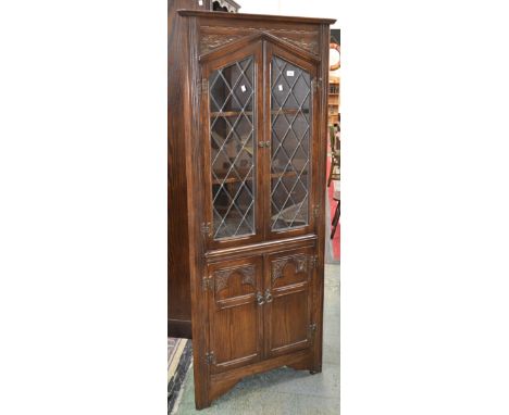 A contemporary oak floor standing corner cupboard, two lead glazed doors to top, two carved panel doors to base.