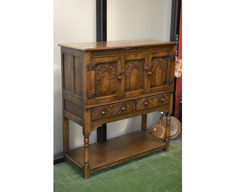 A monastic oak cabinet, oversailing top, three carved panel doors over two carved front short drawers to top, turned supports