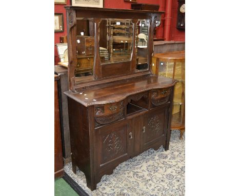 An Arts and Crafts oak mirror back sideboard, shaped oversailing top, recess flanked by bowfront carved drawers over two door