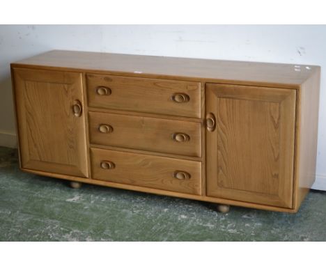 An Ercol Windsor sideboard, light elm and ash, three drawers flanked by cupboards, on caster feet (badge in door Hunters of D