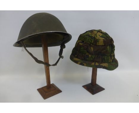 Two British Army helmets with liners, chin straps and camouflaged covers.