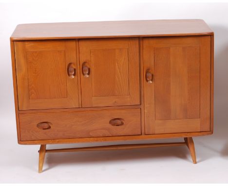 A 1960s Ercol blond elm compact sideboard, having twin upper cupboard doors flanked by single longer cupboard and single long